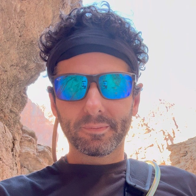 Jon, co-founder of Desert Drip, in sunglasses and a headband, close up in a canyon with a hydration pack tube over his shoulder