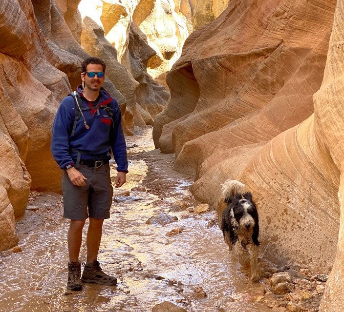 Jon, co-founder of Desert Drip, hiking a red-rock slot canyon with his dog, a hydration pack on his back